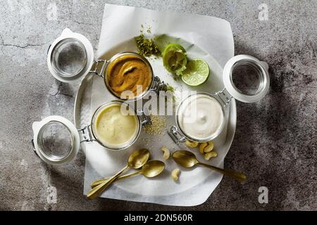 diversi tipi di salse in vasetti di vetro. con pistacchi, cashews e vegan mayo su uno sfondo di pietra Foto Stock