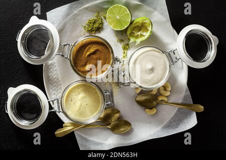 diversi tipi di salse in vasetti di vetro. con pistacchi, cashews e vegan mayo su uno sfondo di pietra Foto Stock