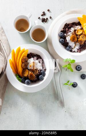 Dolce colazione caraibica di porridge di riso nero con latte di cocco e mango, banane fritte. Sana cucina giamaicana. E caffè Foto Stock