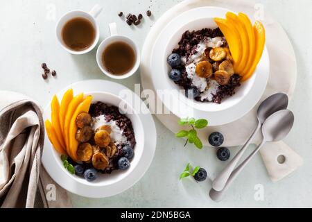 Dolce colazione caraibica di porridge di riso nero con latte di cocco e mango, banane fritte. Sana cucina giamaicana. E caffè Foto Stock