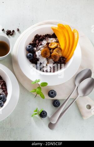 Dolce colazione caraibica di porridge di riso nero con latte di cocco e mango, banane fritte. Sana cucina giamaicana. E caffè Foto Stock