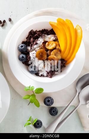 Dolce colazione caraibica di porridge di riso nero con latte di cocco e mango, banane fritte. Sana cucina giamaicana. E caffè Foto Stock