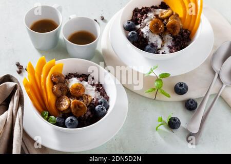 Dolce colazione caraibica di porridge di riso nero con latte di cocco e mango, banane fritte. Sana cucina giamaicana. E caffè Foto Stock