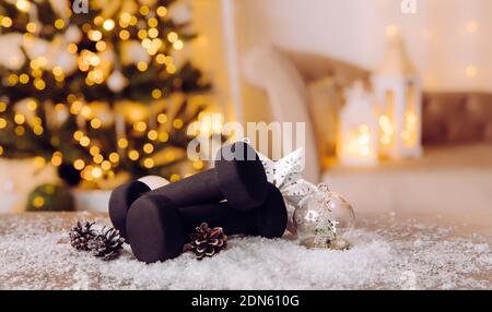 Manubri neri con ornamenti natalizi e neve offuscata albero di Natale sullo sfondo. Stile di vita sano durante il periodo di festa di Natale concetto. Foto Stock