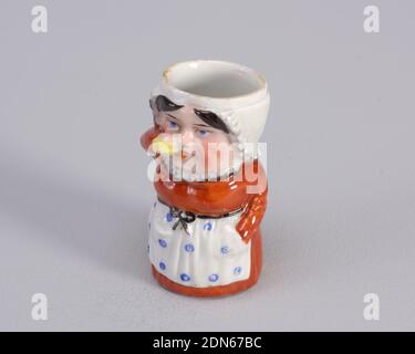 Matchsafe, porcellana, personaggio di donna che beve da bottiglia gialla. Il personaggio indossa un abito ruggine con una volata bianca intorno al collo e un grembiule bianco con grandi puntini blu. La mano della figura è in una tasca del grembiule., fine del diciannovesimo secolo, contenitori, arti decorative, matchsafe Foto Stock
