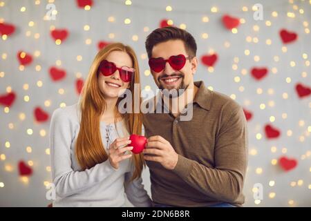 Ritratto di felice giovane coppia che indossa divertenti occhiali da sole a forma di cuore e. Goditi San Valentino Foto Stock