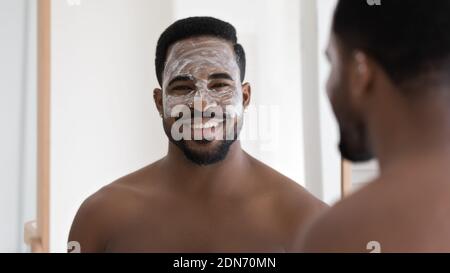 Sorridente giovane anni '30 afroamericano applicando maschera idratante sul viso. Foto Stock