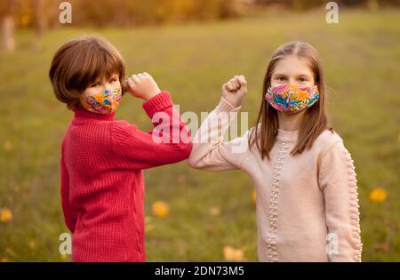 Children in protected mask on covid-19 lockdown, greeting. Friends shaking elbows outdoors. Greeting with elbows. Stop handshakes. Coronavirus epidemi Stock Photo