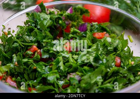 Primo piano su insalata Tabbouleh fatta con prezzemolo, pomodori ciliegini, cipolla, limone, olio d'oliva e basilico Foto Stock