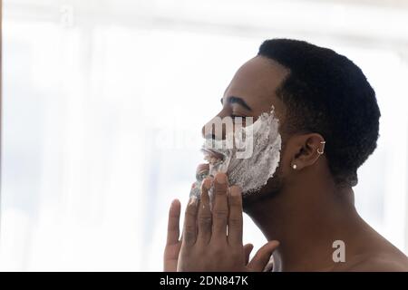 Felice giovane uomo di razza mista pulizia viso con scrub schiumoso. Foto Stock