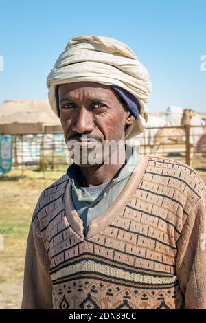 Il tradizionale Pastore dei cammelli si trova di fronte al cammello nell'area desertica di al Sarar - Arabia Saudita. 17 gennaio 2020. Foto Stock