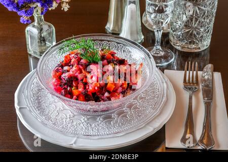 Transparent glass bowl with vinaigrette of various boiled vegetables beet, potato, carrot, onion, dill, cabbage, served on the table of restaurant. Foto Stock