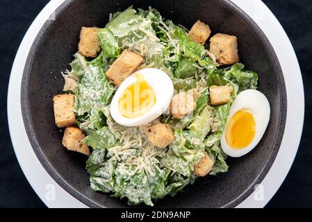 Vista dall'alto della ciotola della Caesar Salad con condimento con parmigiano, crostini e uova sode. Foto Stock