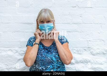 Donna che indossa una maschera Coronavirus che copre su uno sfondo bianco chiaro durante la pandemia di Covid-19, mettendola pronta per la fine del blocco per Foto Stock