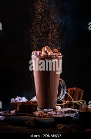 Bicchiere di cioccolata calda, bevanda di cacao cosparsa di cacao in polvere. Sfondo scuro. Concetto invernale di cibo e bevande con spazio fotocopie Foto Stock