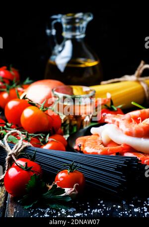 Spaghetti neri, pomodori ciliegini, vino bianco, gamberetti, calamari, vita morta in basso, fuoco selettivo Foto Stock