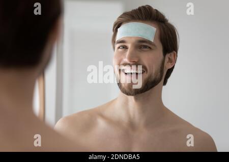 Felice giovane bell'uomo che applica la patch idratante sulla fronte. Foto Stock