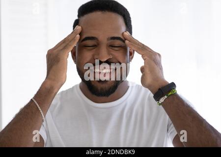 Felice misto razza uomo africano facendo massaggio viso rilassante. Foto Stock