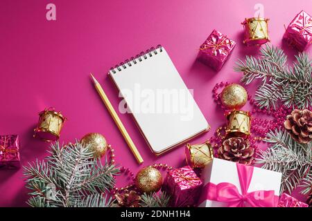 Pulisca il blocco note bianco con la matita intorno alle decorazioni di Natale su sfondo rosa. Pianificazione, lista dei desideri e risoluzione 2021. La vista dall'alto Foto Stock