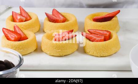 Torte biscottate con frutti di bosco freschi, cioccolato e panna pesante montata. Donna che prepara dessert, coppette di biscotti con fragole e mirtilli, c Foto Stock