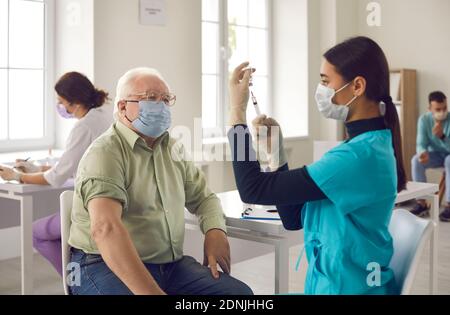 Paziente anziano in attesa di ottenere un colpo e guardare giovane medico che prepara il vaccino Foto Stock