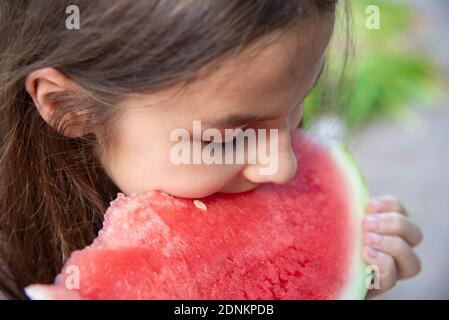 Una ragazza mangia un grande pezzo di rosso succosa anguria primo piano. Il concetto di mangiare vitamine di frutta. Foto Stock