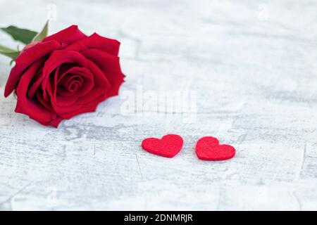 Due cuori rossi e rosa rossa su sfondo bianco di pietra. Regalo romantico per San Valentino. Amore. Messa a fuoco morbida. Spazio di copia. Vista dall'alto Foto Stock