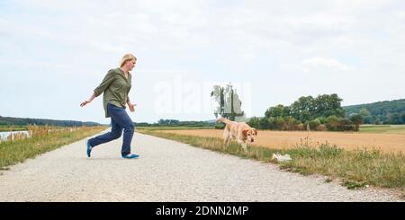Donna e Labrador Retriever. Donna cammina fino al cane, che corre a spazzatura. La donna vuole impedire al cane di mangiare rifiuti Foto Stock