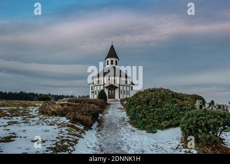 Piccola cappella bianca rurale Tesarovska con cimitero nel villaggio di Korenov, Jizera montagne, Repubblica Ceca. Vista del paesaggio invernale al tramonto Foto Stock