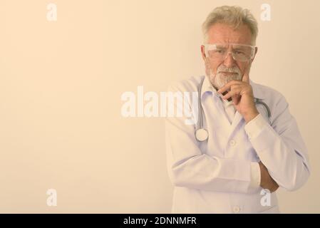 Studio shot di bello senior uomo barbuto medico pensando indossando occhiali protettivi contro uno sfondo bianco Foto Stock