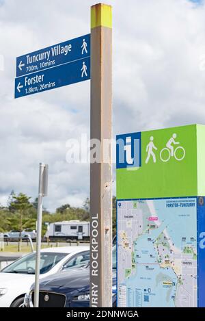 Un cartello stradale, un cartello e una mappa che forniscono una distanza a piedi e in bicicletta e il tempo per raggiungere le località di Forster Tuncurry, nuovo Galles del Sud, Australia Foto Stock