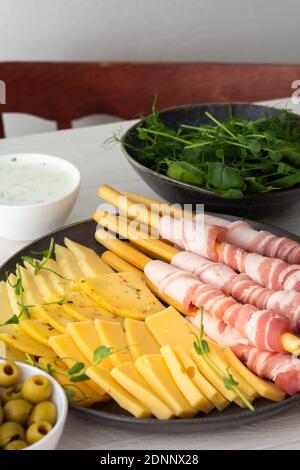 Pane grissini con pancetta, diversi tipi di formaggio e germogli di piselli, salsa e olive su fondo bianco di legno Foto Stock