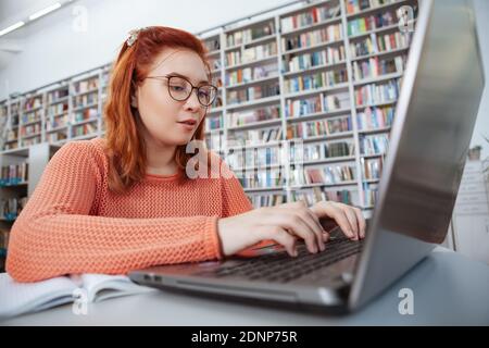 Young woman working on her laptop at the library. Female student using computer, studying for exams Stock Photo