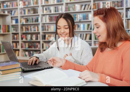 Allegro college femmina amici ridere mentre studiano insieme alla biblioteca. Educazione, concetto di amicizia Foto Stock