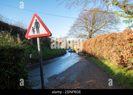 Pedoni a piedi triangolo rosso cartello stradale con adulto che tiene le mani con un bambino su una stretta strada di campagna vicino a una scuola, Regno Unito Foto Stock