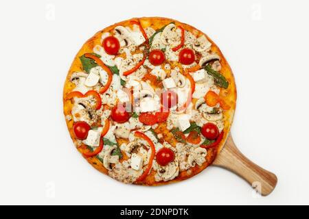 Deliziosa pizza vegetariana servita su un piatto di legno, gli ingredienti sono salsa di firma, basilico, mozzarella, champignons, peperoni, pomodori ciliegini, formaggio feta. Poster promozionale pizzeria. Foto Stock