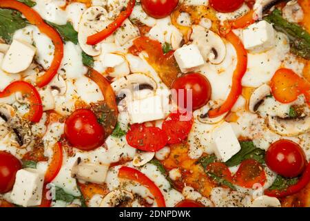 Deliziosa pizza vegetariana servita su un piatto di legno, gli ingredienti sono salsa di firma, basilico, mozzarella, champignons, peperoni, pomodori ciliegini, formaggio feta. Poster promozionale pizzeria. Foto Stock