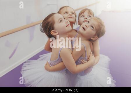 Adorabili bambine in leotards e tutu gonne abbracciare, guardando via gioiosamente. Gruppo di simpatici ballerine giovani che si divertono dopo la lezione di balletto, copia Foto Stock