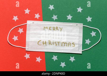 Maschera facciale bianca non medica su sfondo rosso e verde con stelle bianche e testo di Merry Chrismas. Foto Stock