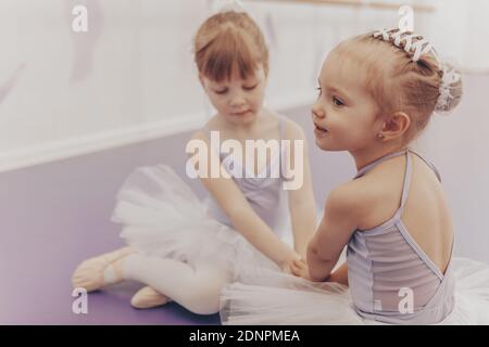 Bella bambina seduta sul pavimento con la sua migliore amica a scuola di balletto. Carino ballerine in leotards e tutu gonne che riposano dopo la dancin Foto Stock