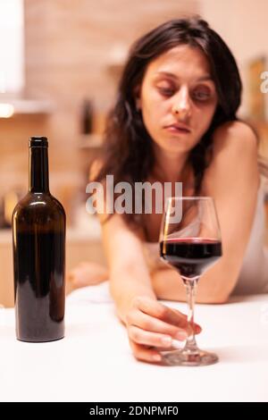 Donna con dipendenza da alcol tenendo la mano su un bicchiere di vino rosso deluso e triste. La malattia della persona infelice e l'ansia si sentono esauriti con problemi di alcolismo. Foto Stock