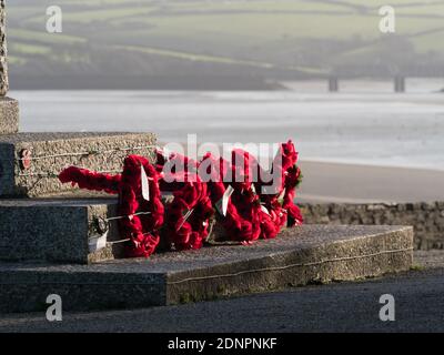 Una fila di corone di papavero rosso è stata posata alla base di un memoriale con estuario e ponte sullo sfondo a Padstow, Cornovaglia. Foto Stock