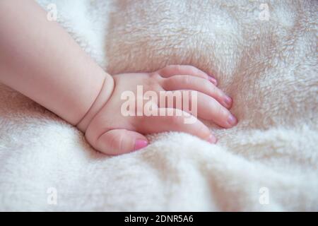 Mano del bambino su una coperta morbida e soffice beige. Unghie sulla mano di una bambina dipinta con smalto rosa unghie Foto Stock