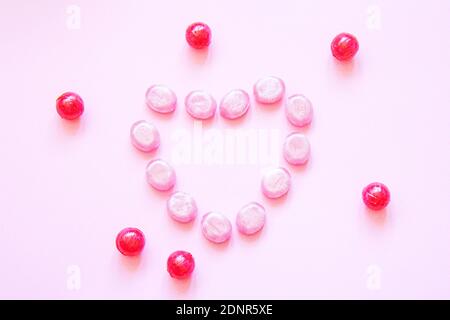 Lollipop multicolore su sfondo colorato. 14-febbraio concetto. Gustosi cuori dolci in caramello isolato su sfondo rosa. Disposizione piatta Foto Stock