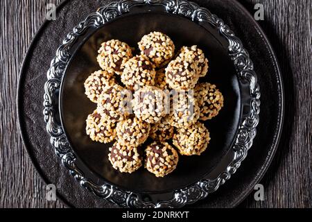 Tartufi di cioccolato scuro rivestiti da mandorle tritate serviti su un piatto nero su sfondo di legno scuro, vista dall'alto, primo piano Foto Stock