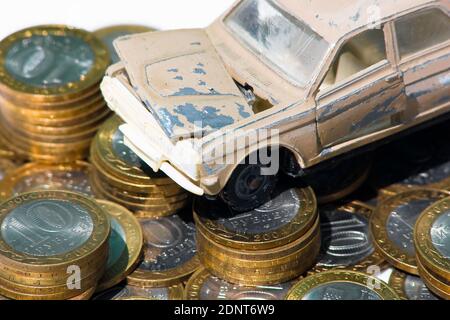 Il costo di manutenzione di una vecchia auto. Un modello di una vecchia auto è in piedi su monete. Il concetto di manutenzione costosa di un'automobile vecchia o del relativo smaltimento Foto Stock