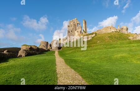 Il principale sentiero acciottolato che conduce al Castello di Corfe in una giornata di sole con erba verde brillante e senza persone. Corfe Castle, Wareham, Dorset, Inghilterra. Foto Stock