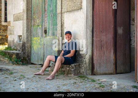 Ritratto di uomo moderno seduto fuori dal vecchio edificio rurale Foto Stock