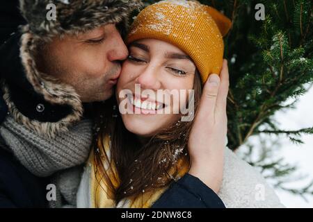 L'uomo baciando la donna in una guancia davanti ad un abete in inverno. Foto Stock