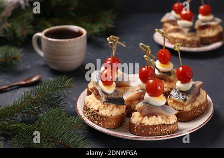 Tartine con aringhe salate, formaggio, uova di quaglia e pomodori ciliegini su crostini di segala e tazza di caffè su fondo scuro. Formato orizzontale Foto Stock